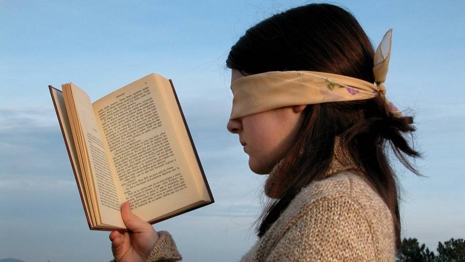 Geblinddoekte vrouw met leesboek in de hand.